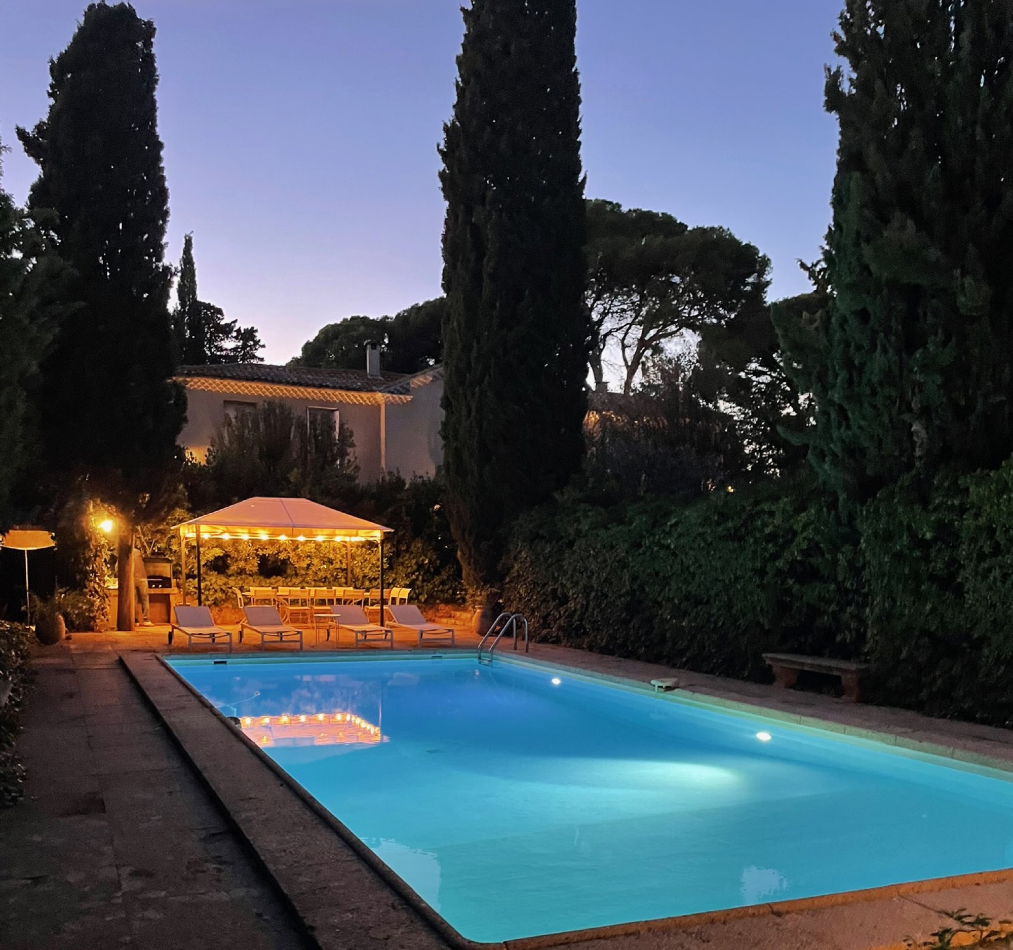 The pool at dusk, lit between the cypresses
